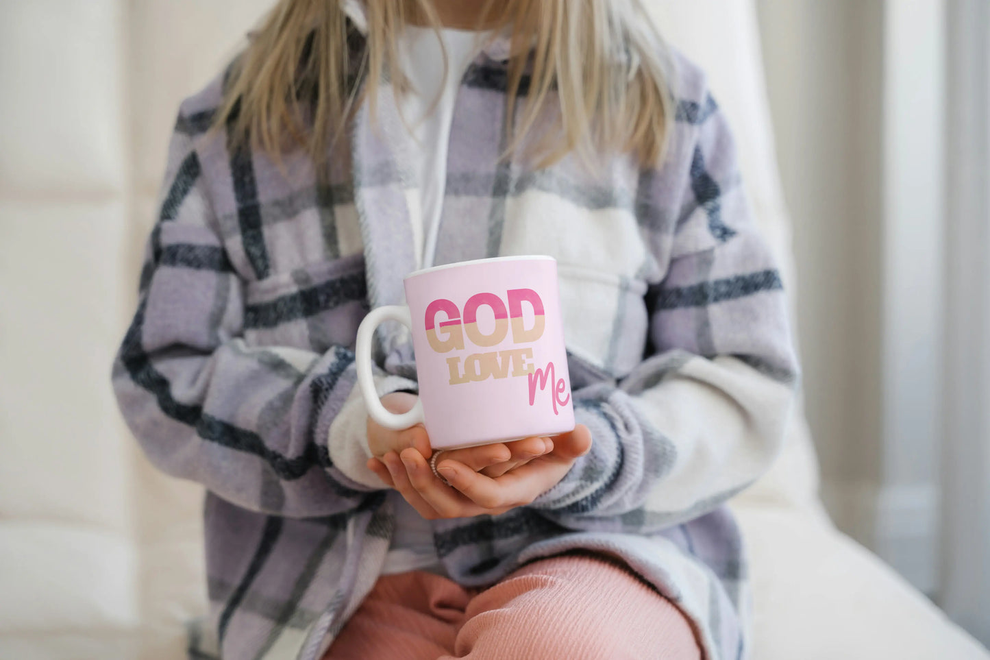 Person holding a mug with 'GOD LOVE ME' text in a cozy indoor setting
